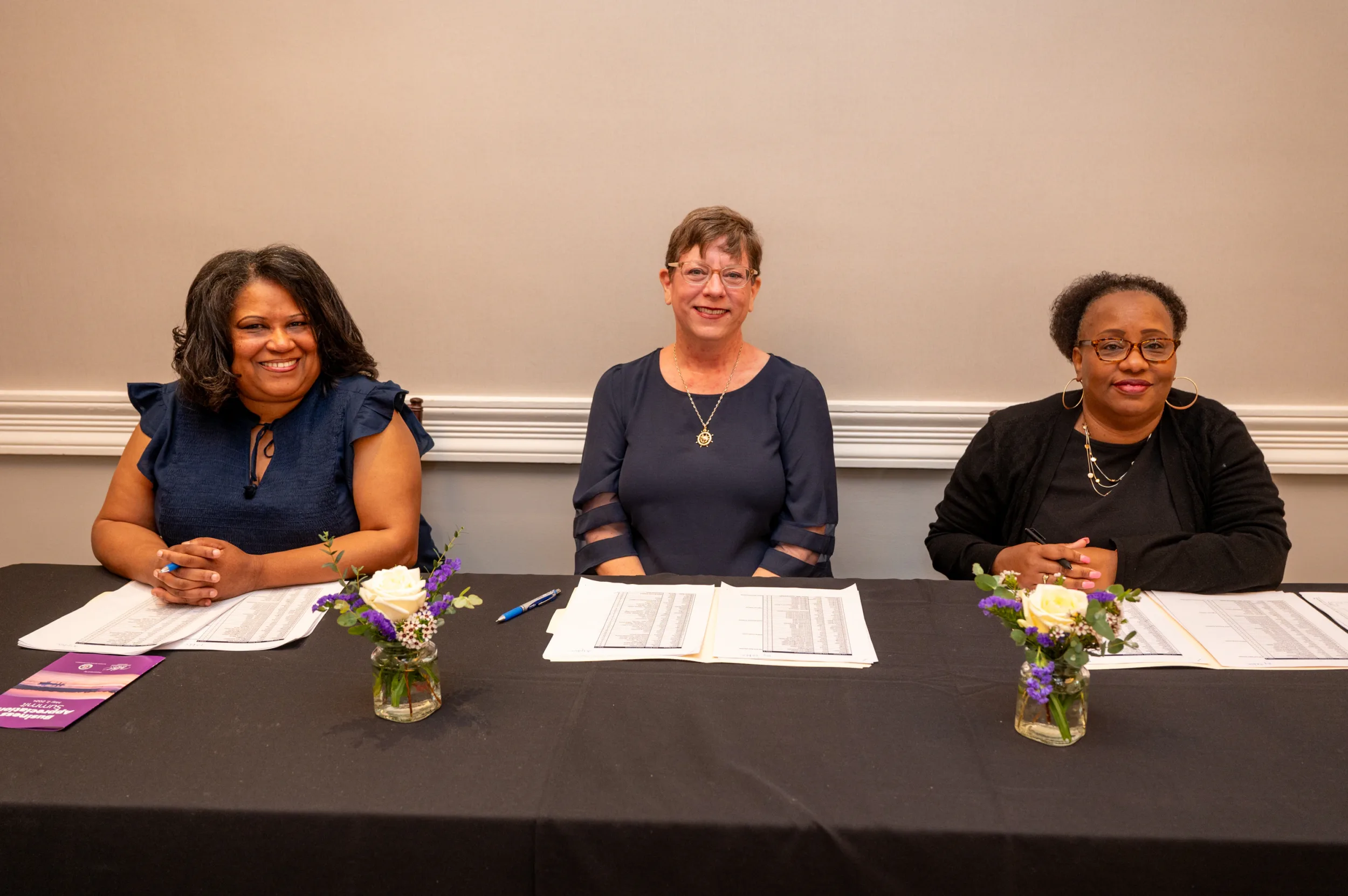 Three people seated at a panel table with name cards and flowers