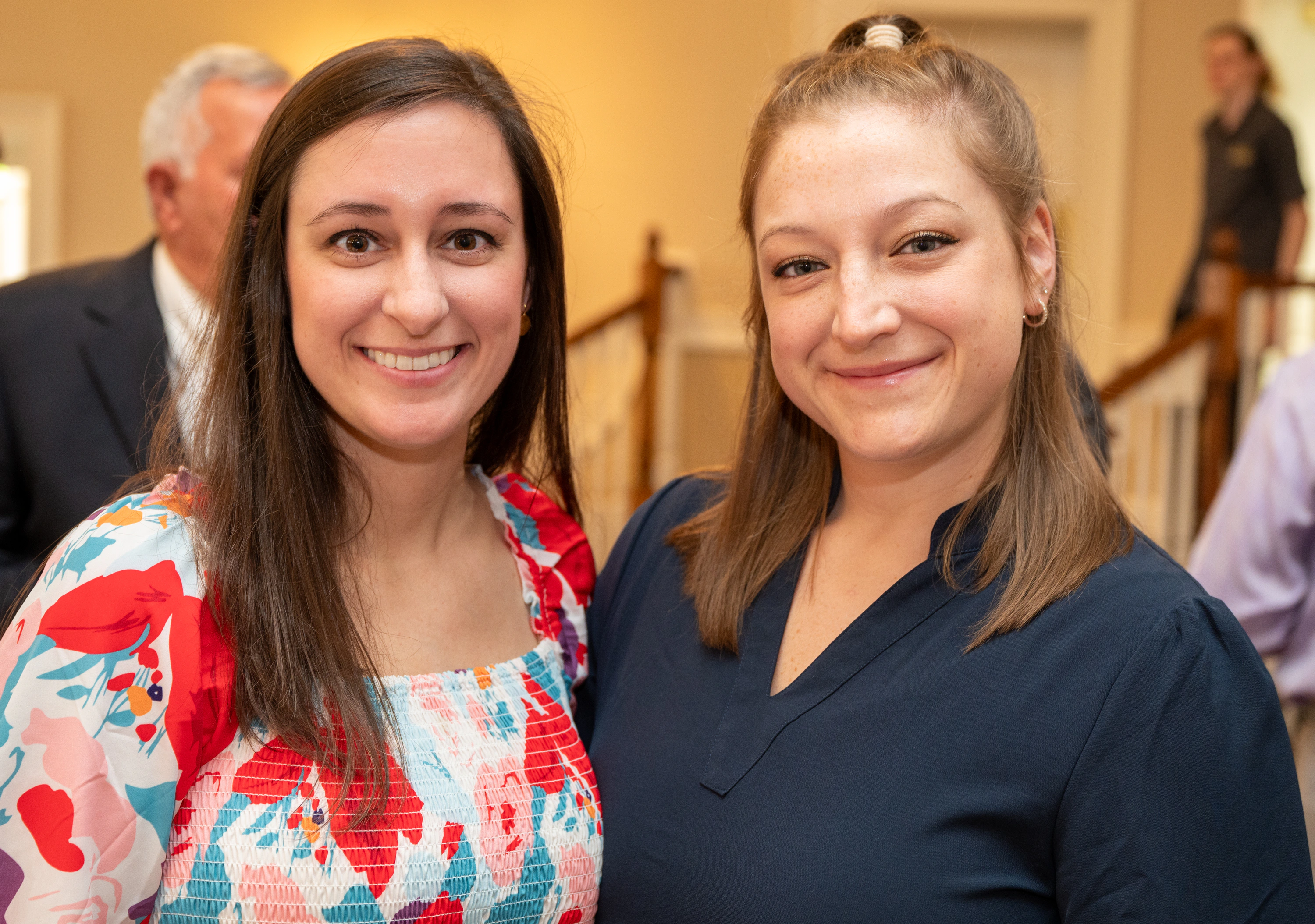 Two women smiling together at an event, one in floral dress and one in navy top