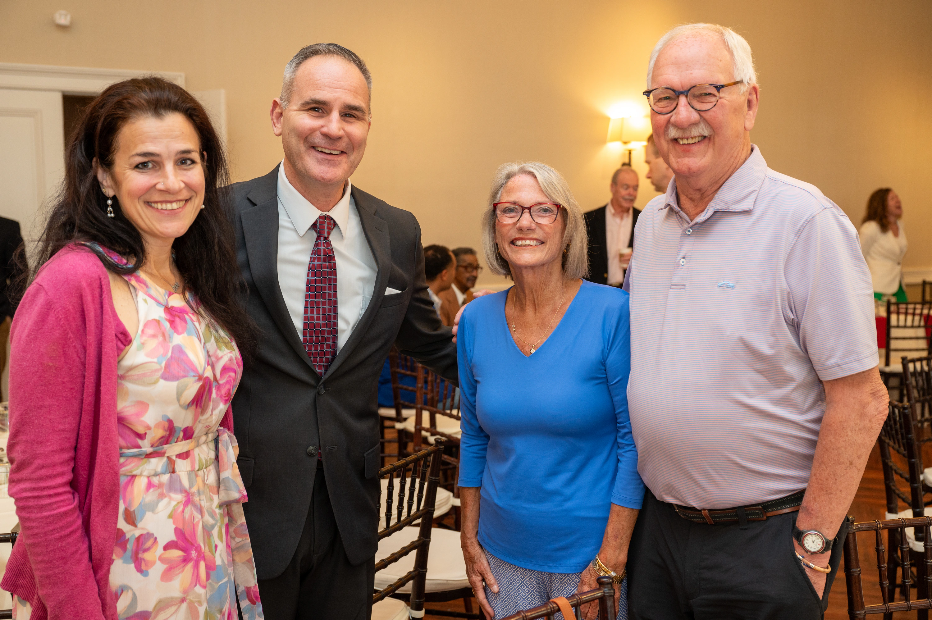 Four people smiling at an event: a man in suit, women in pink and blue, and a man in polo