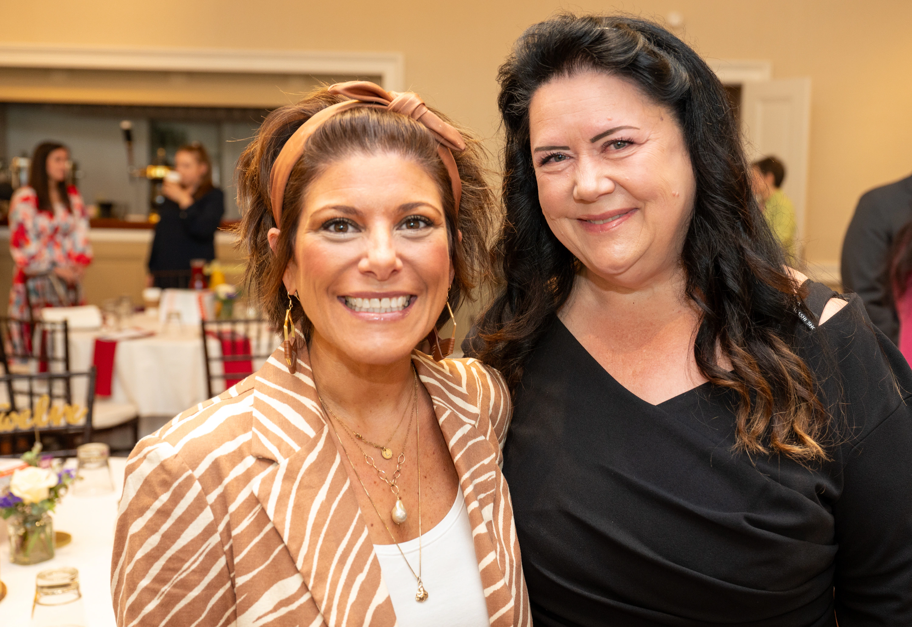 Two women smiling together at an event, one in orange striped jacket