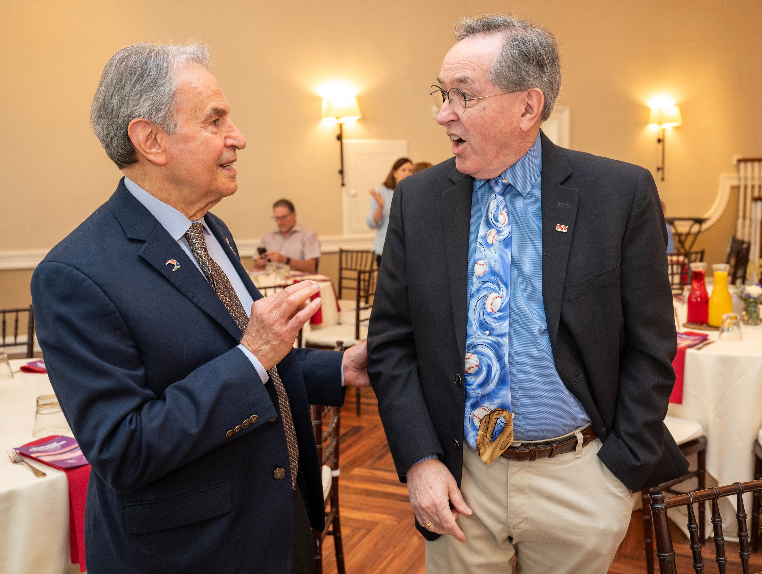 Two older men in suits talking together in a banquet room