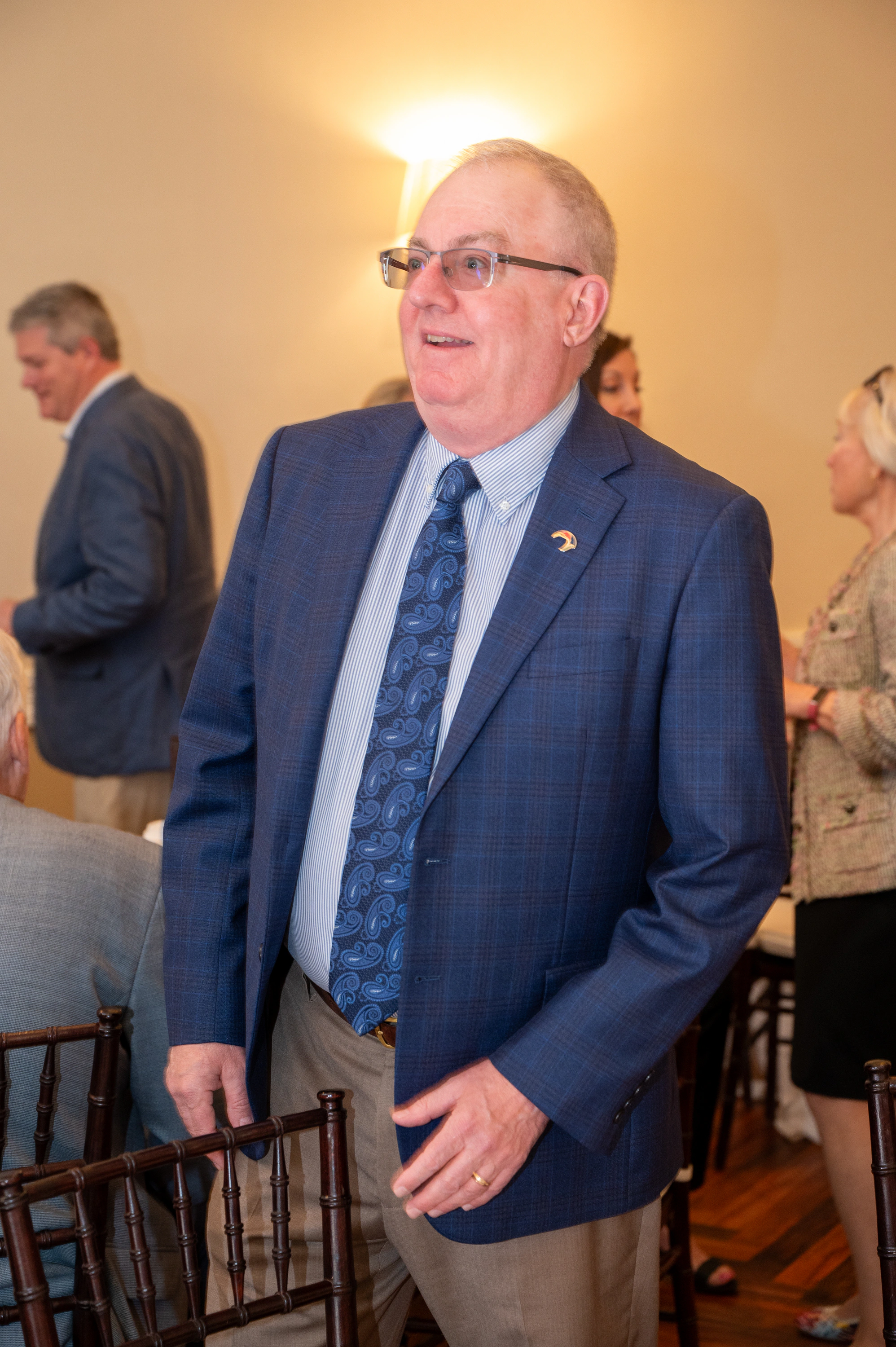 Man in blazer standing in a banquet room with guests behind him