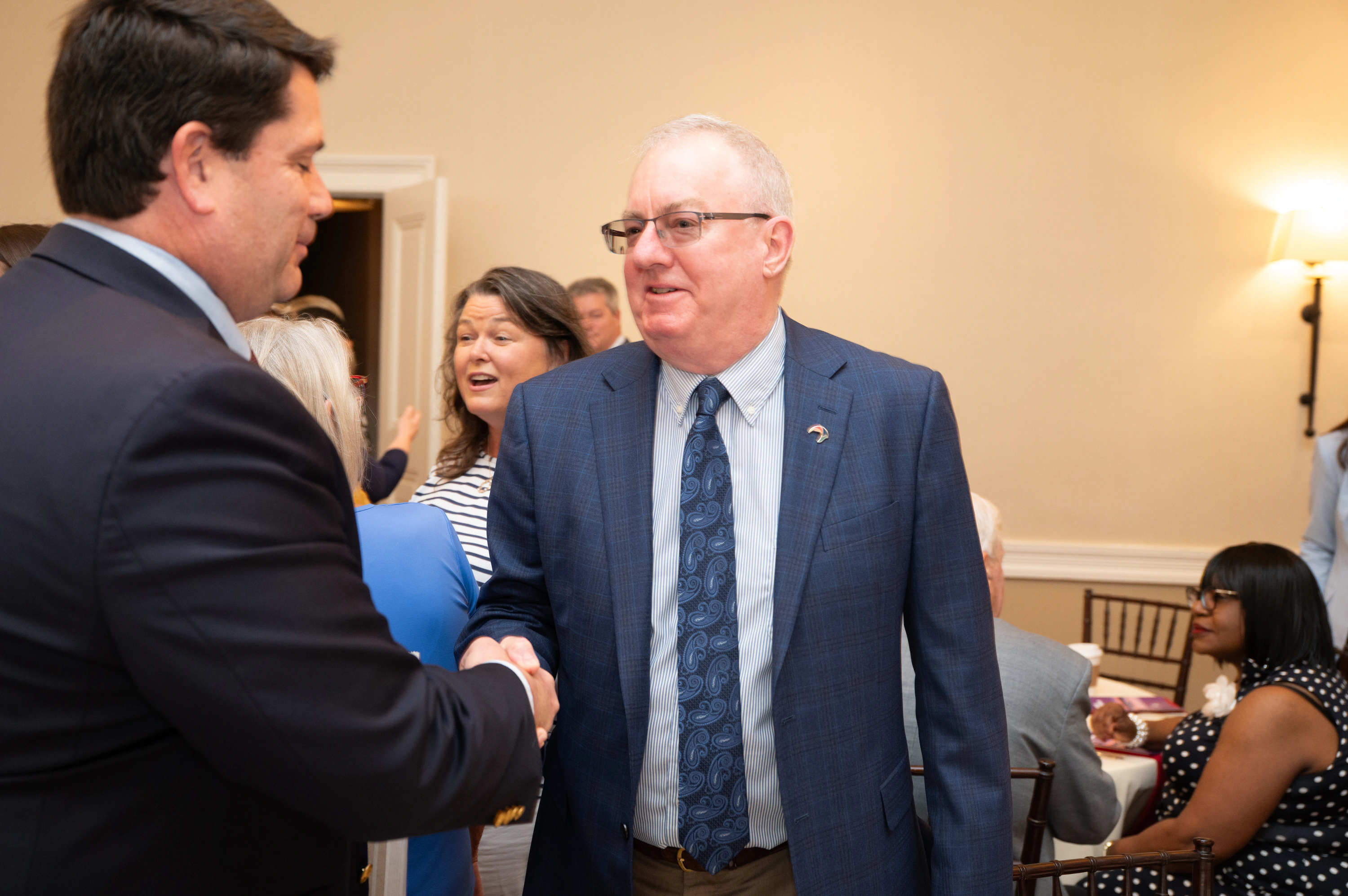 Man in blue suit shaking hands with a man in glasses at an event