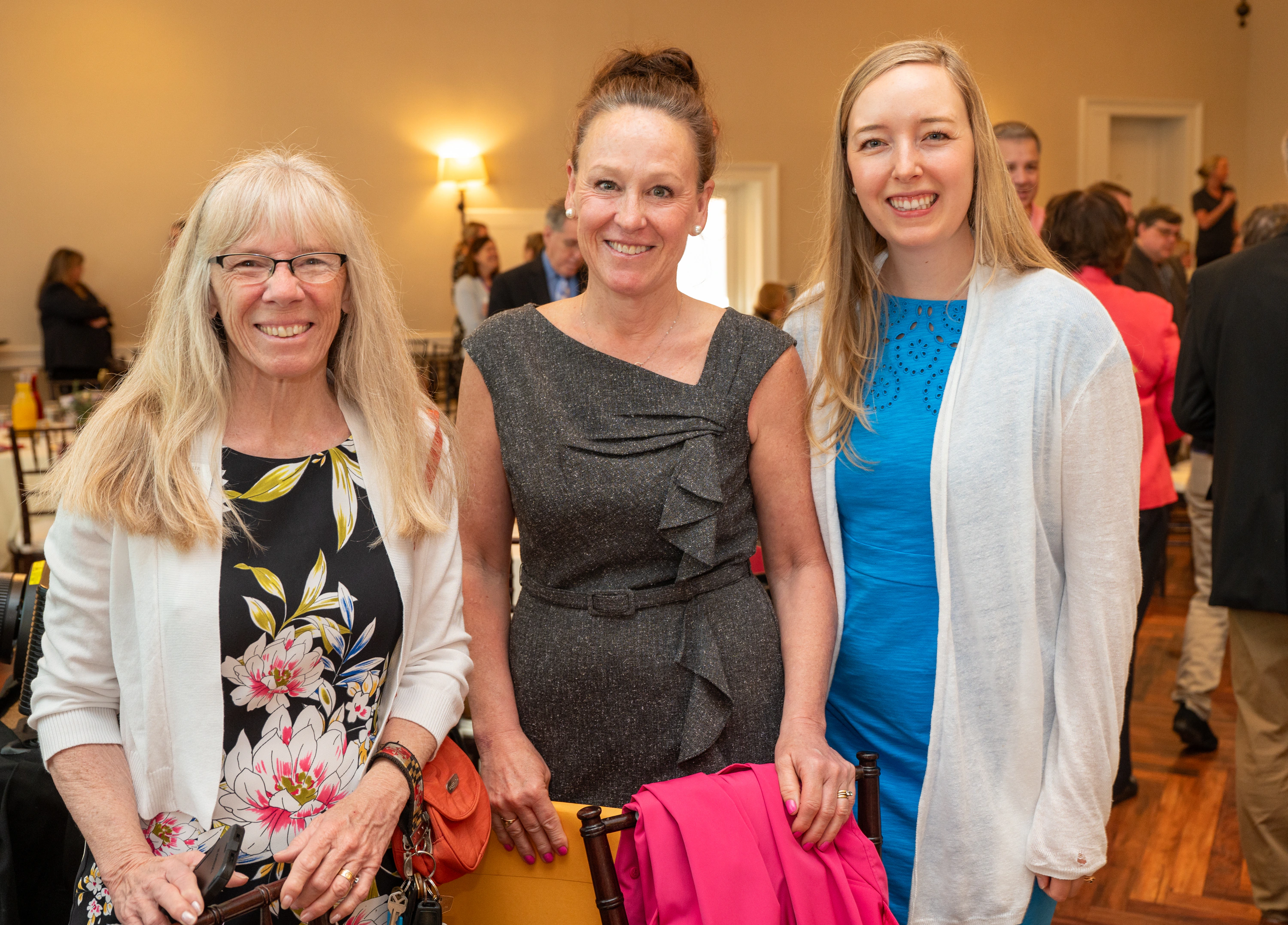Three women posing together at an event, one in a gray dress