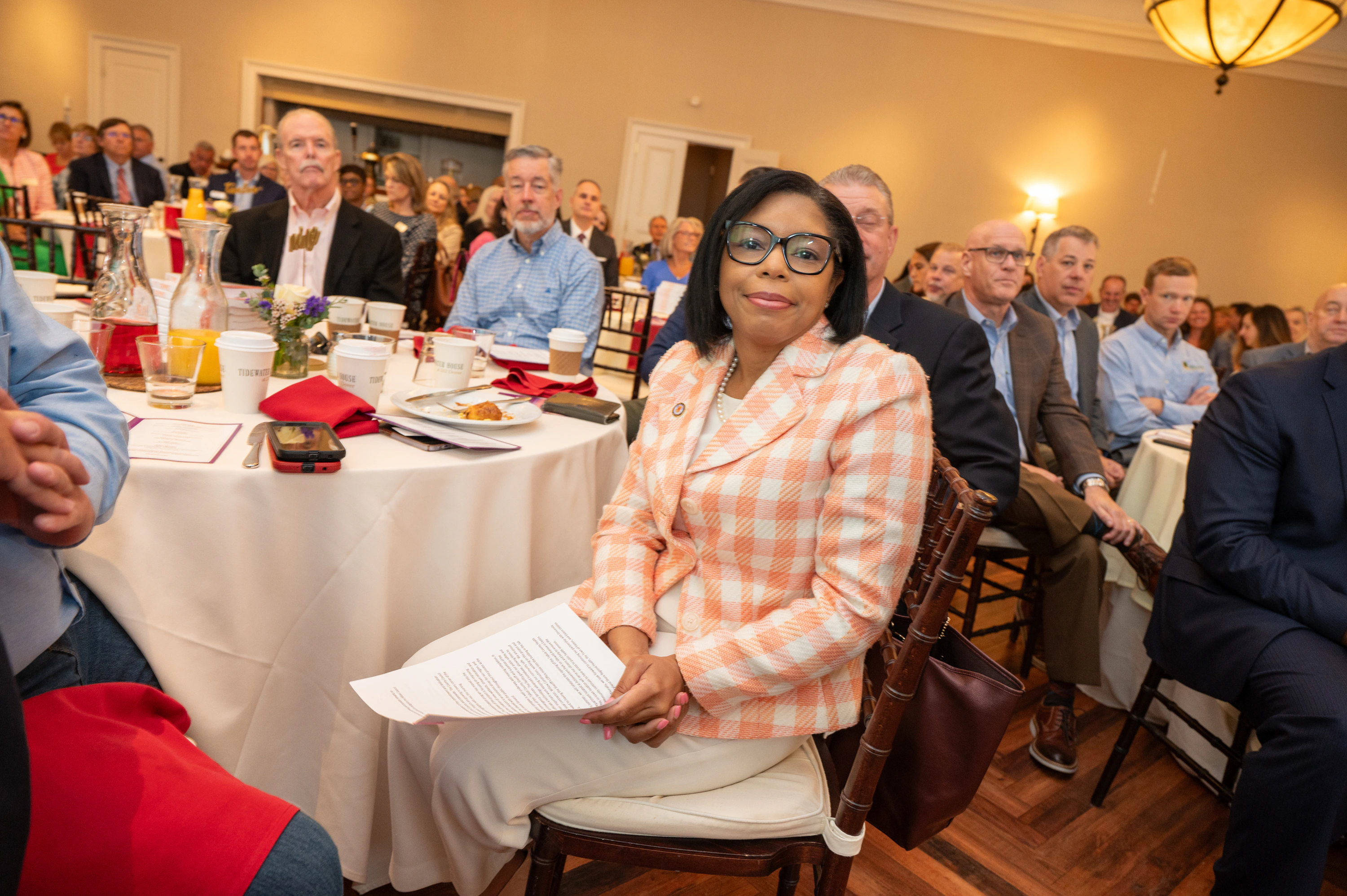 Woman in plaid jacket seated among an audience at a banquet hall
