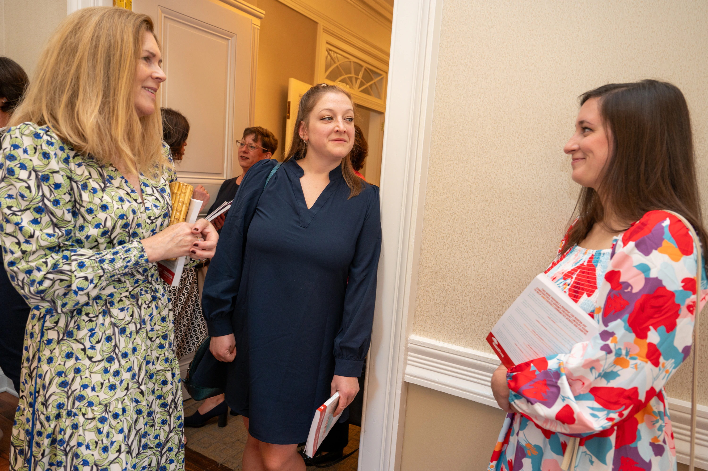 Three women talking in a hallway at an event, one holding papers