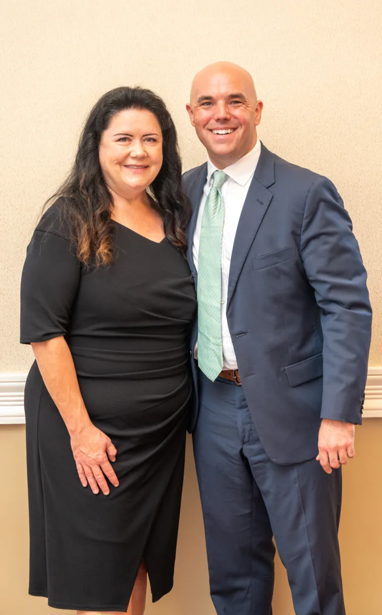 Man and woman smiling and posing in front of a wall at an event