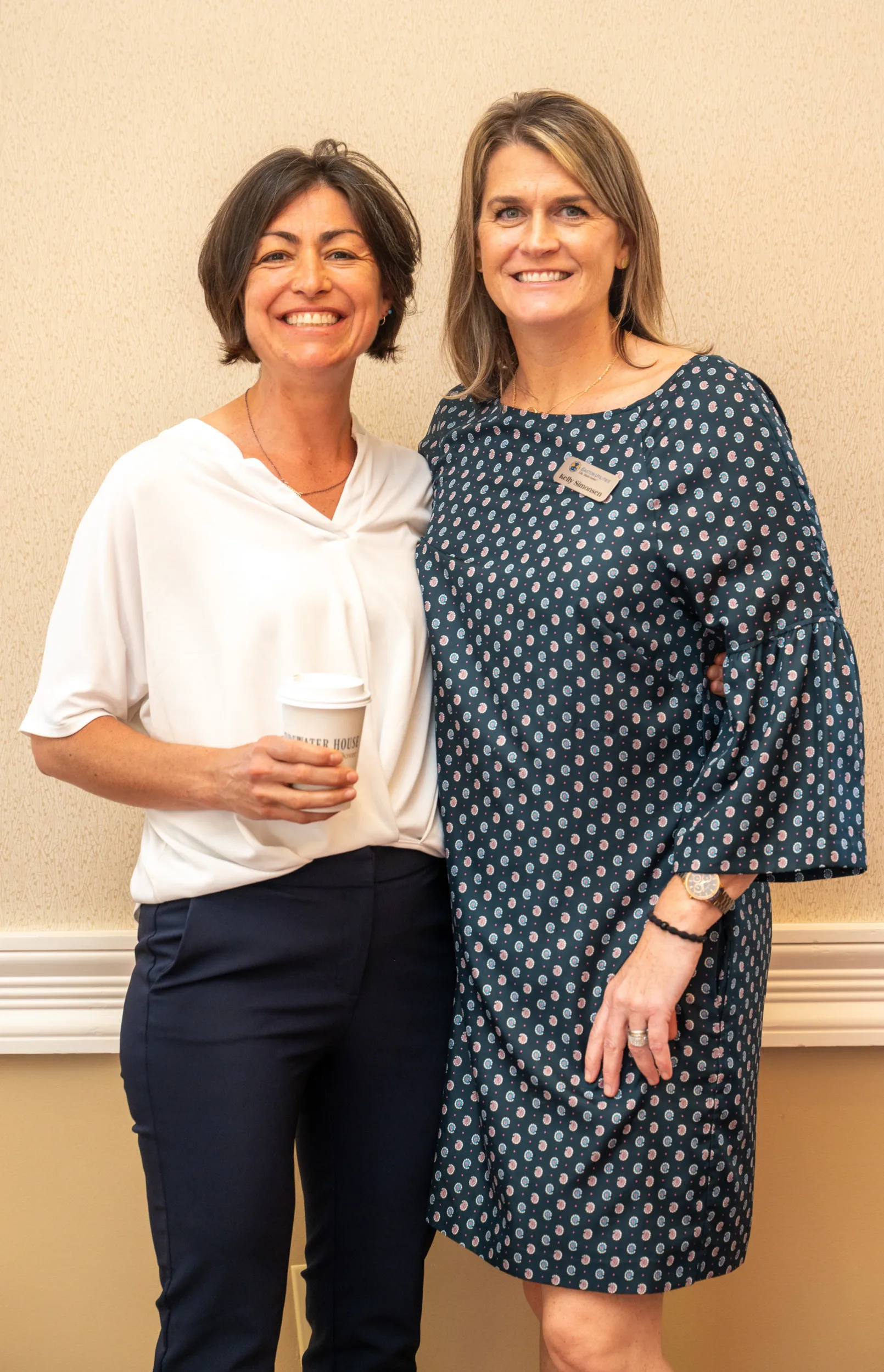 Two women smiling in front of a wall at an event