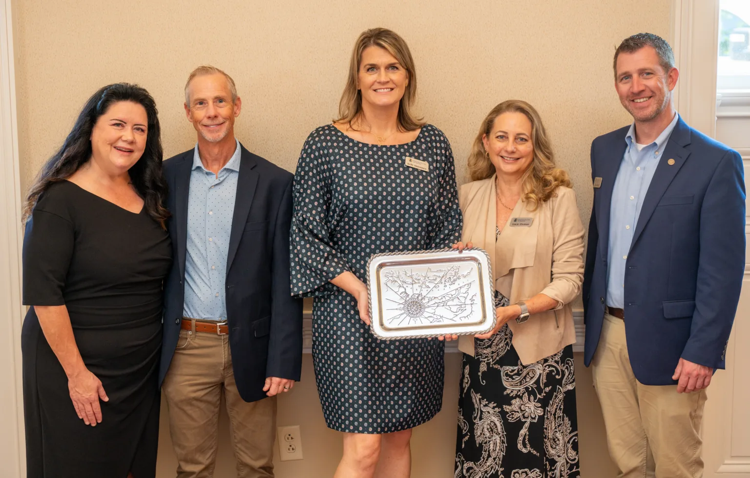 Five people posing with a framed award plaque at an indoor event