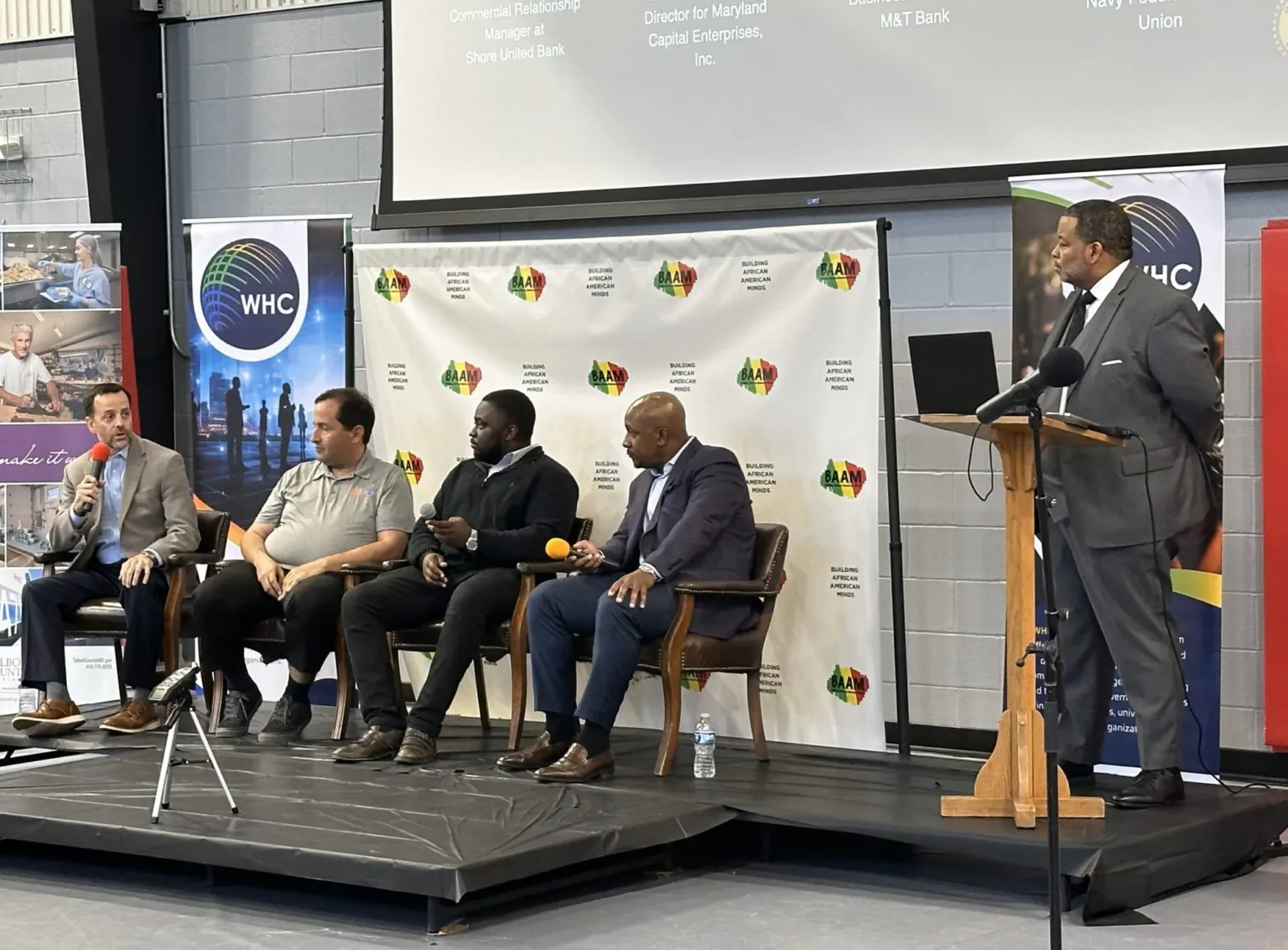 Four panelists seated on a conference stage beside a man at a podium, WHC backdrop