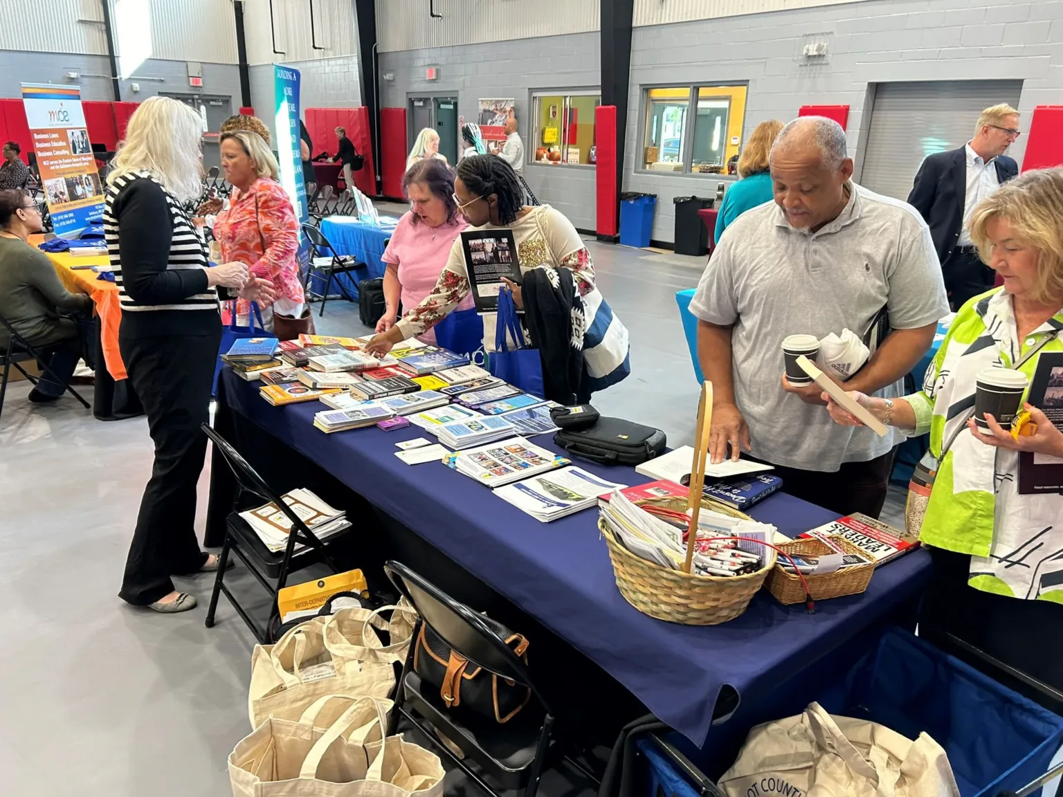 Attendees at exhibitor tables with brochures and baskets at a conference hall