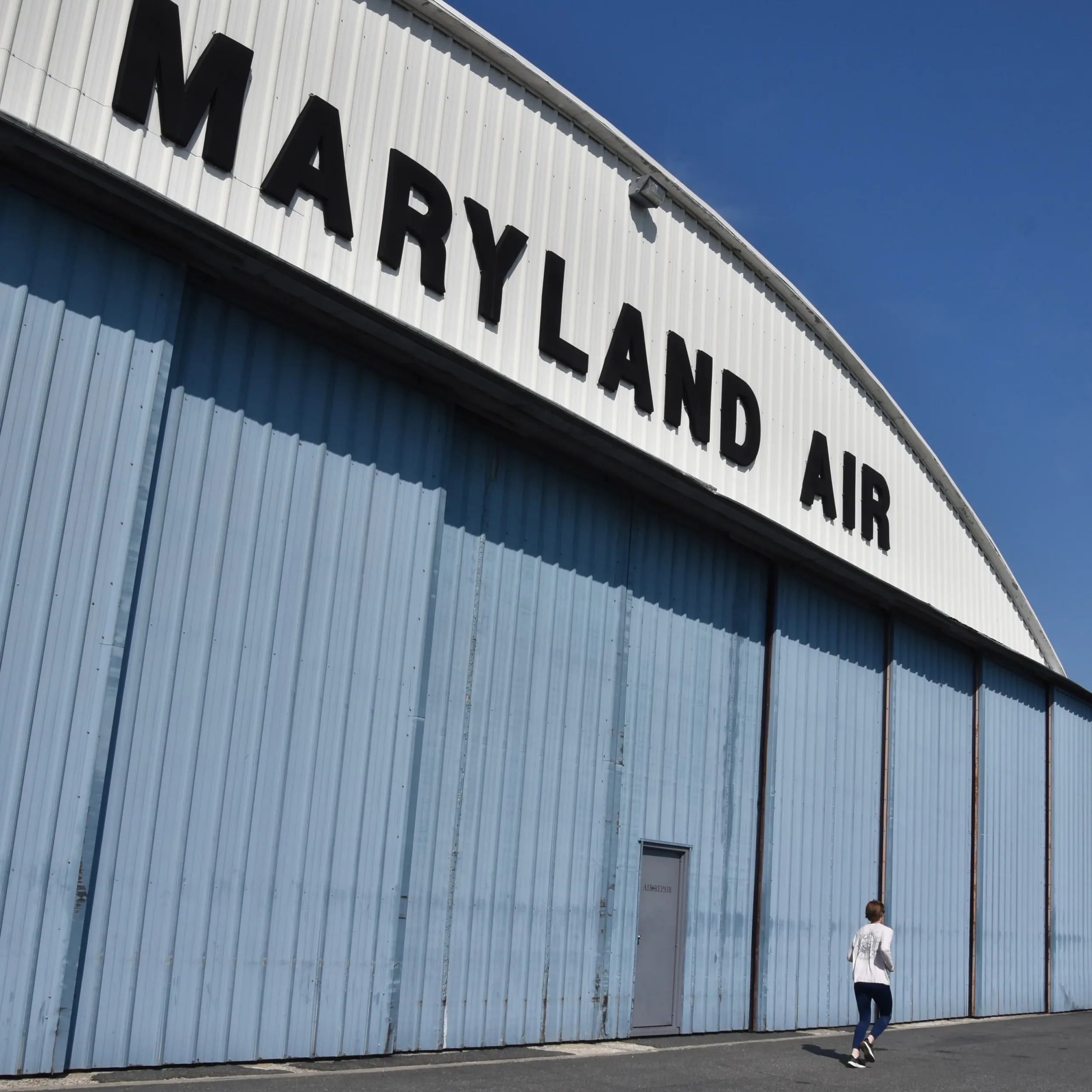 Pedestrian walking past a hangar labeled MARYLAND AIR