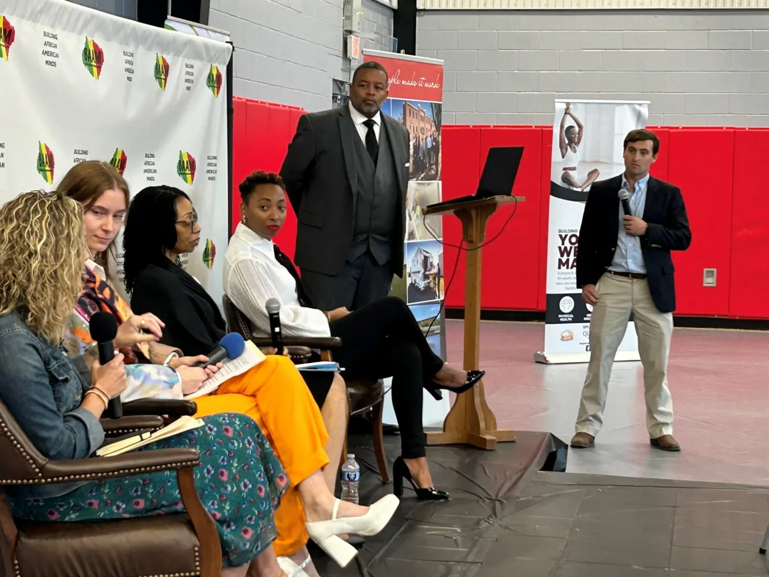 Panelists seated on stage at a WHC event with a man speaking at a podium