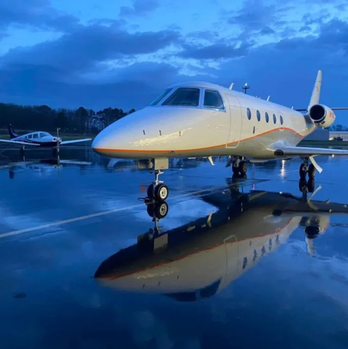 Cream-colored private jet on a wet tarmac at dusk