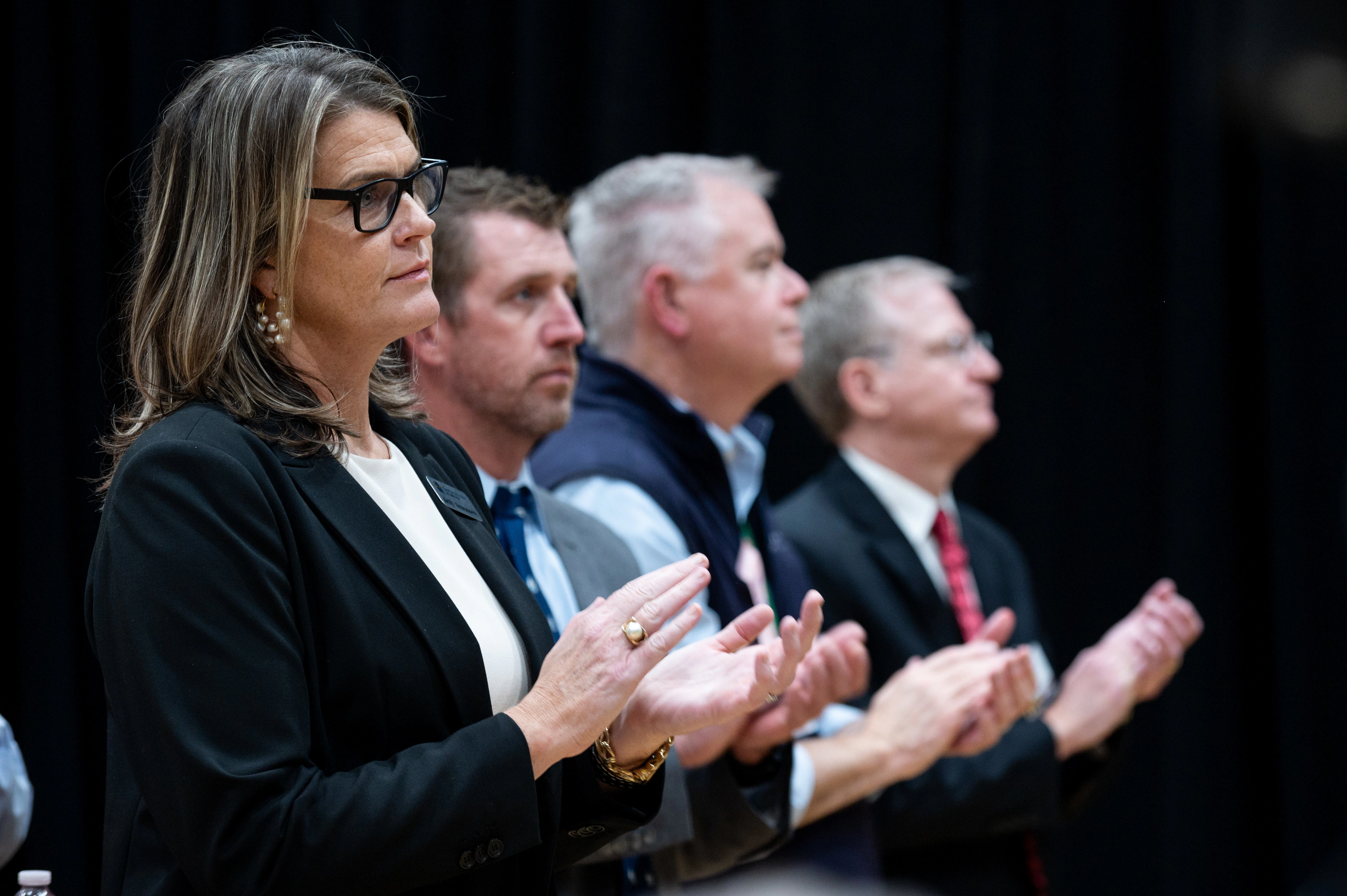 Row of people in dark clothing applauding in front of a black backdrop
