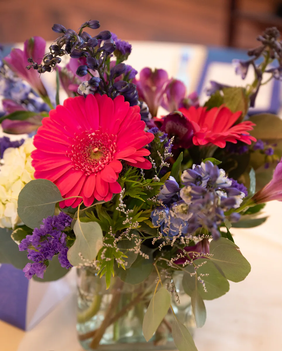 Pink gerbera daisy and purple flowers arranged in a glass vase