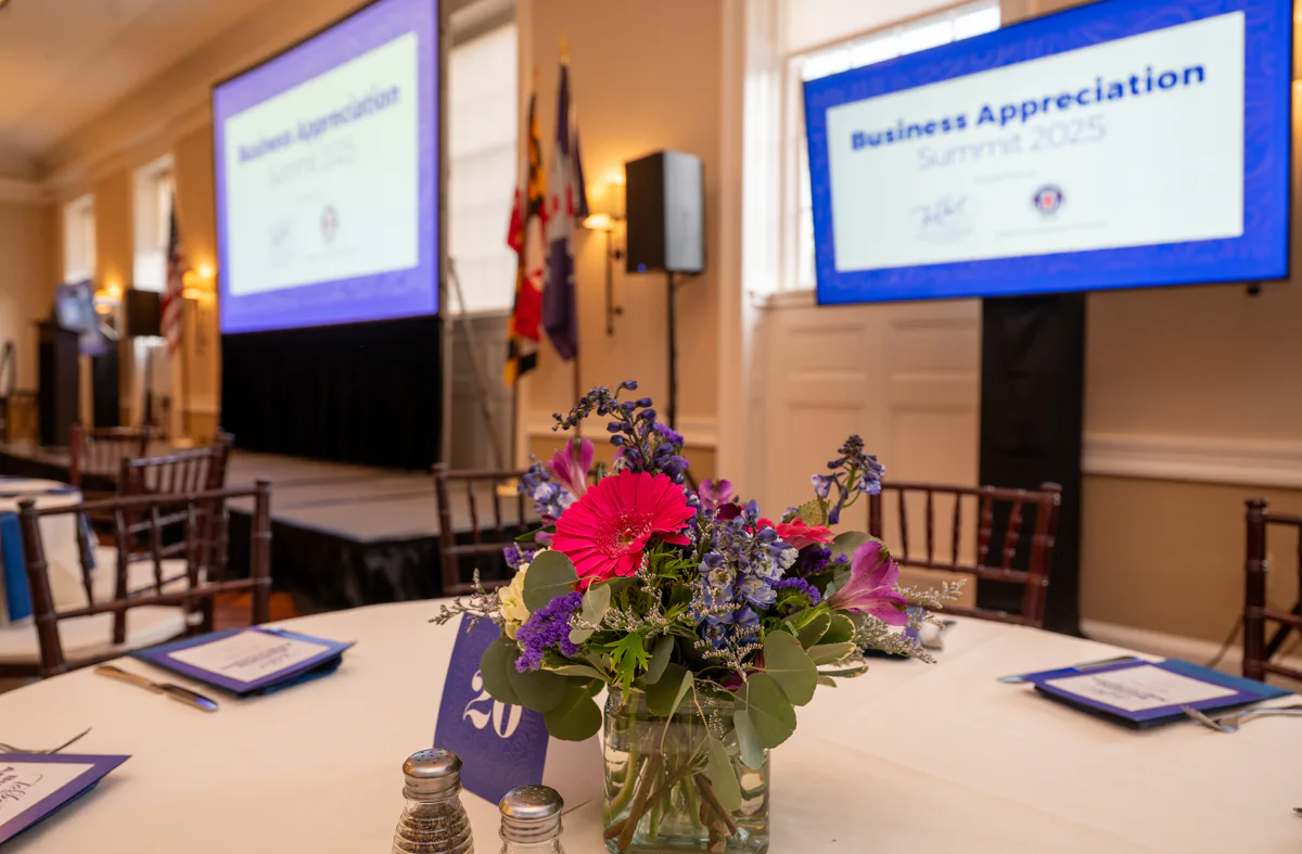 Table centerpiece of purple and pink flowers in front of screens reading Business Appreciation Summit
