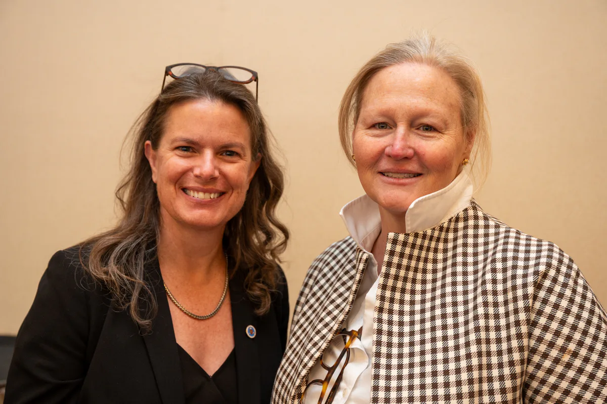 Two women smile side by side, one with sunglasses resting on her head