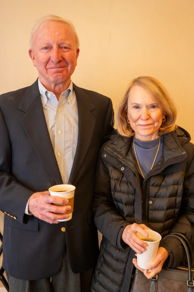 Older man in dark blazer and older woman smile, each holding a coffee cup