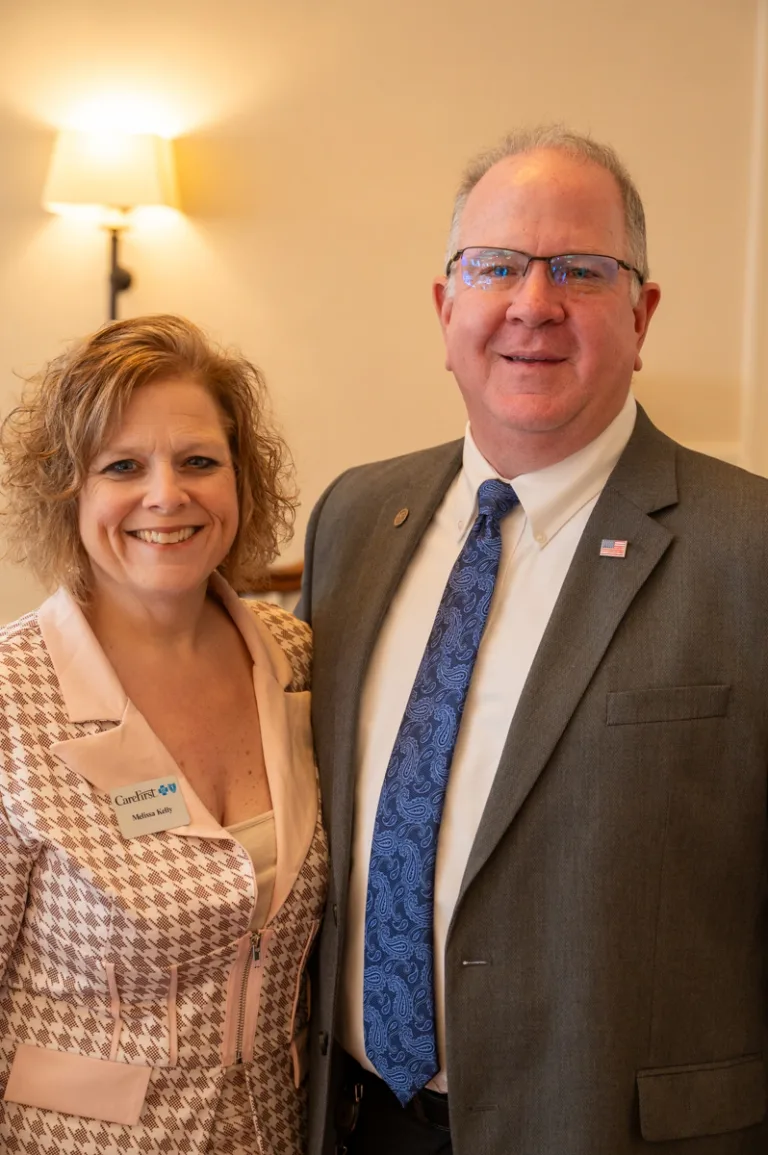 Woman with curly hair and name badge stands beside a smiling man in gray suit