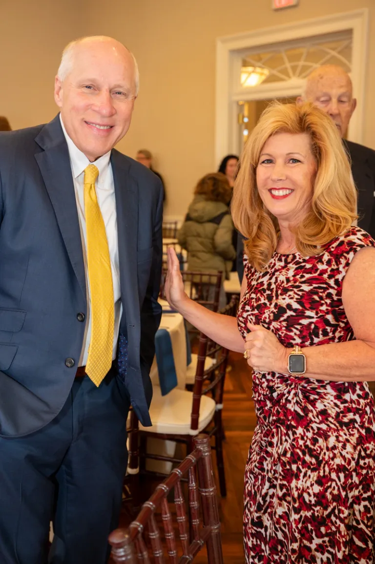 Older man in navy suit and yellow tie stands beside a smiling woman in red dress