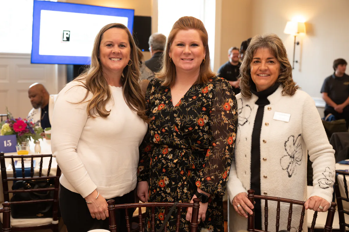 Three women pose in front of a blue screen at a banquet hall