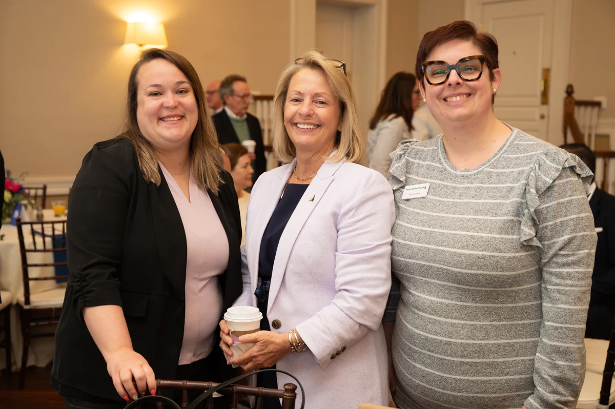 Three women pose together, one holding a coffee cup