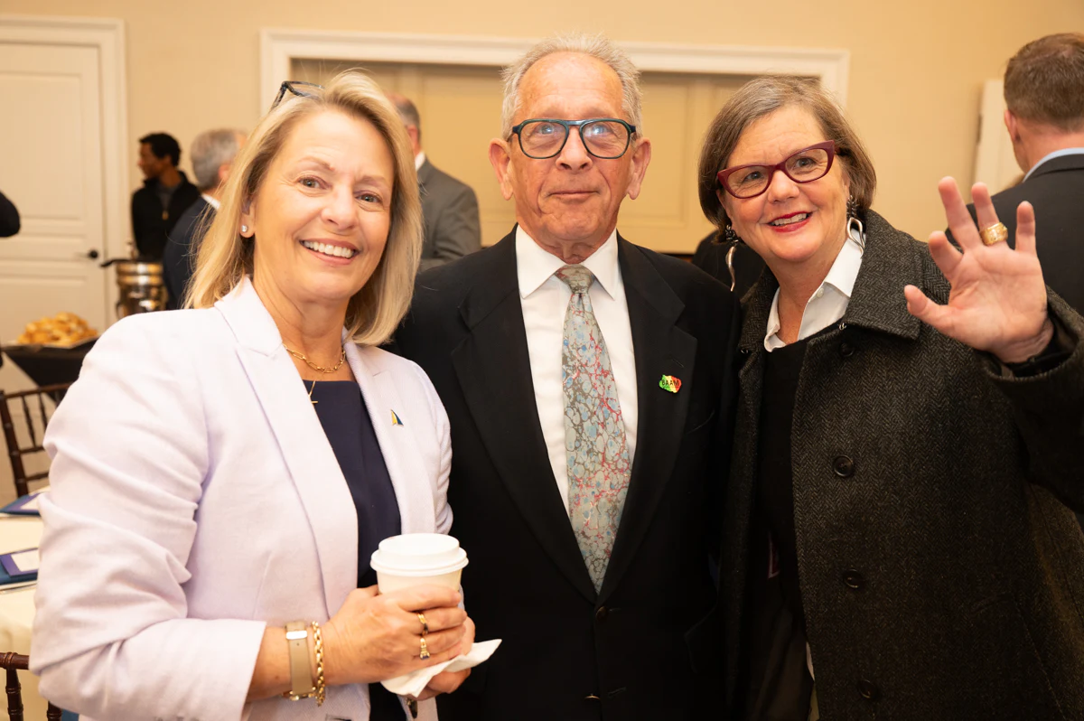 Blonde woman with coffee cup stands with an older man and a woman with glasses