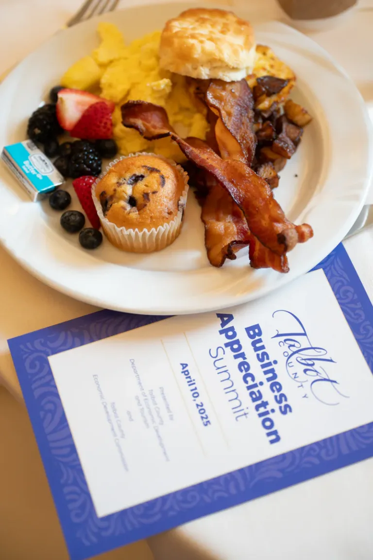Breakfast plate with eggs, bacon, biscuit, and berries beside a Business Appreciation Summit program card