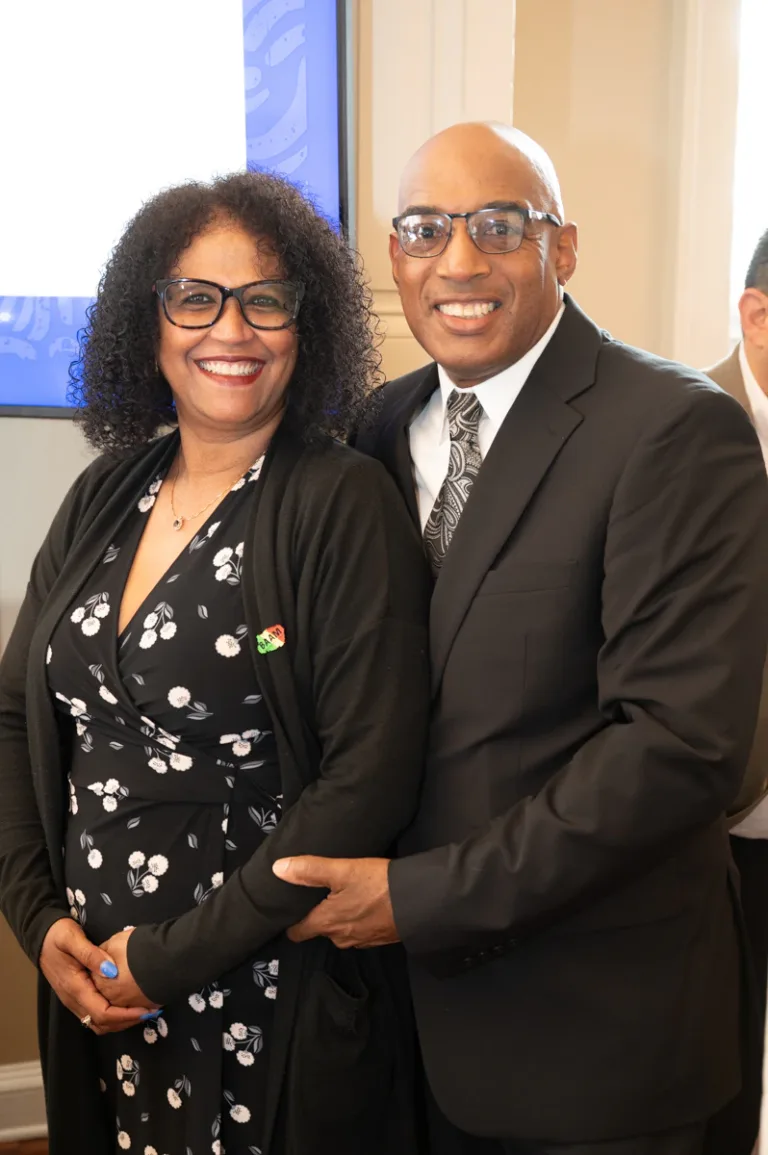 Man in dark suit and woman in black floral dress pose and smile together