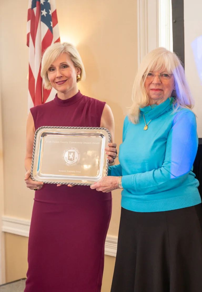 Two women hold a silver engraved tray, one in plum dress and one in aqua sweater