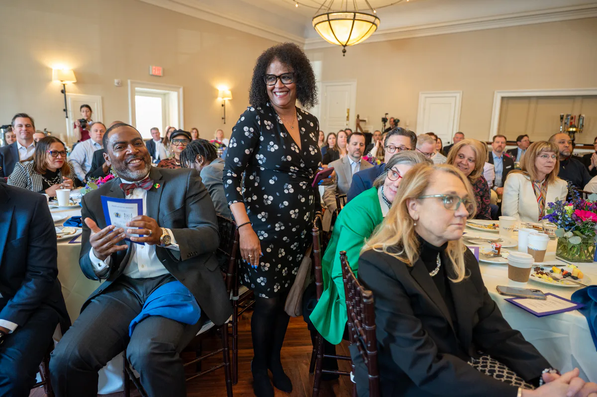 Woman in black floral dress stands among seated guests at a banquet table