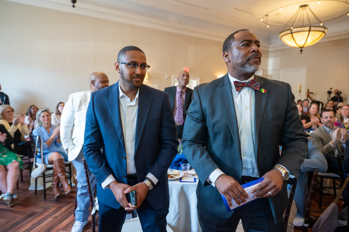 Two men walk through a banquet hall, one wearing a bow tie