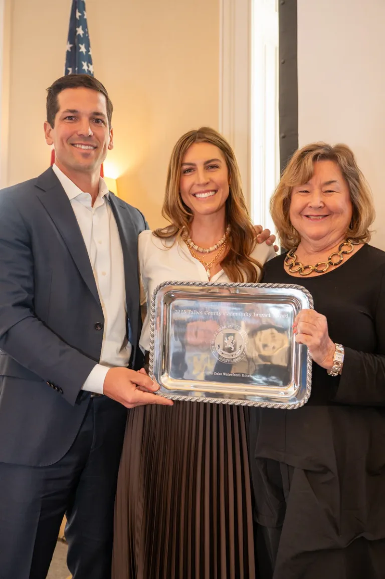 Three people in a formal room hold a silver tray with a framed photo.