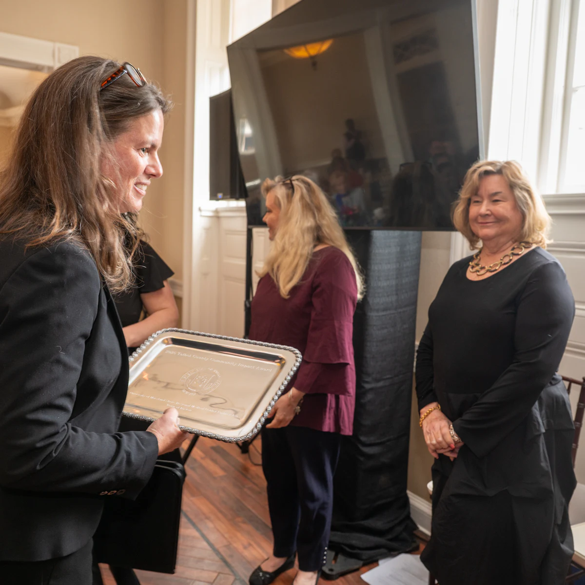 Woman holding a silver tray plaque beside a woman in a black top