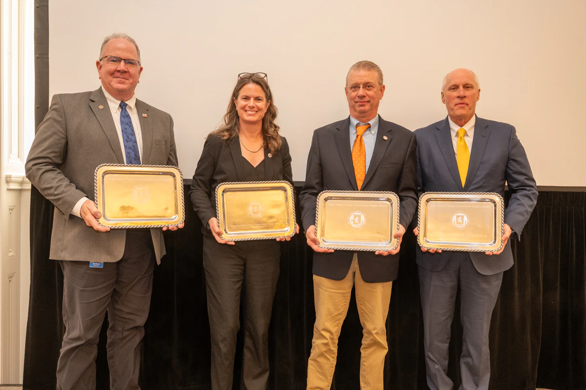 Four award recipients in suits hold gold plaques in a row.