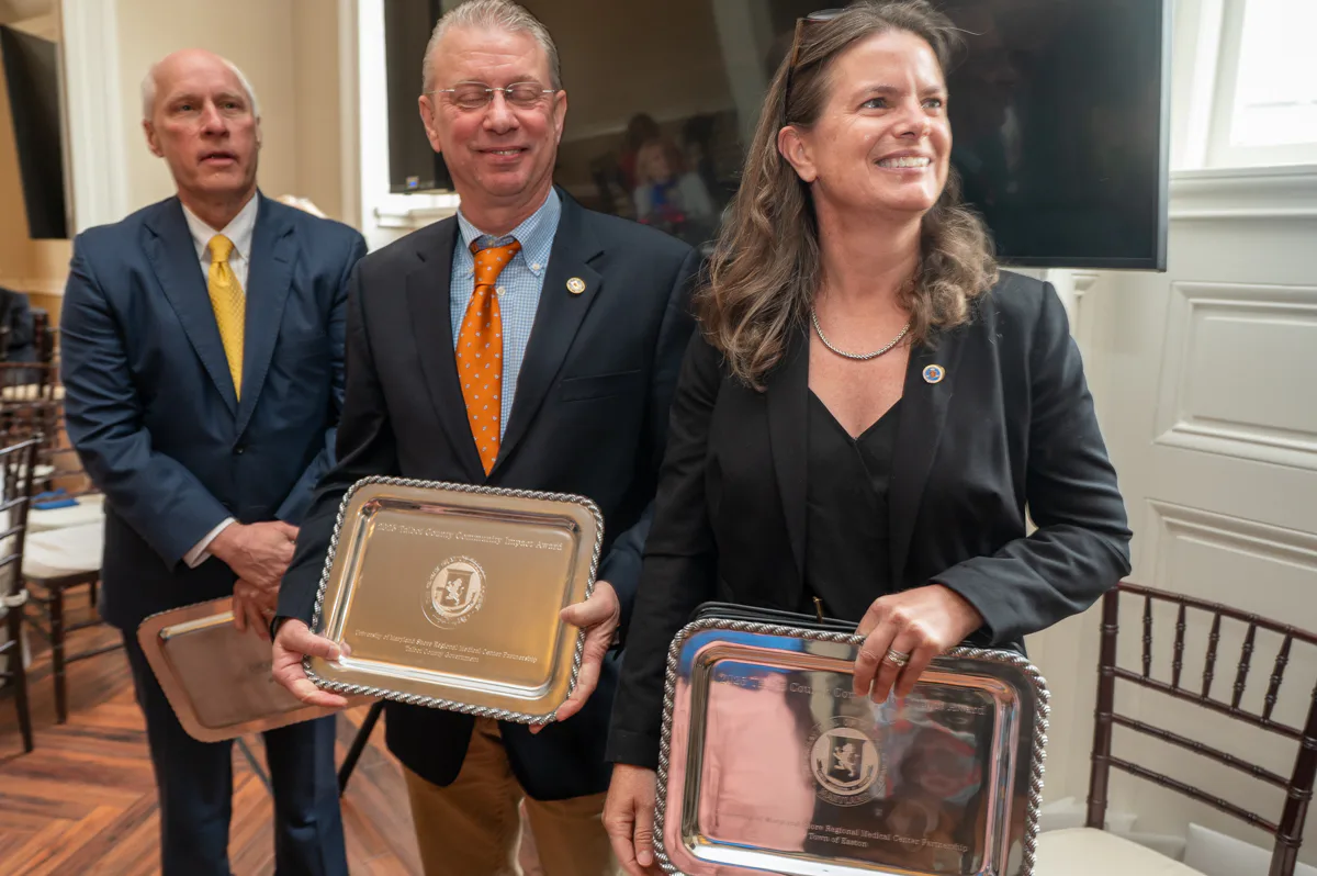 Three men and a woman hold silver award trays in a formal room.