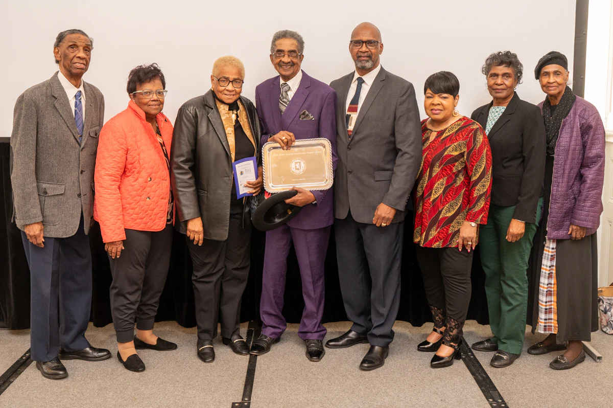 Six people posing with an award plaque in front of a banner