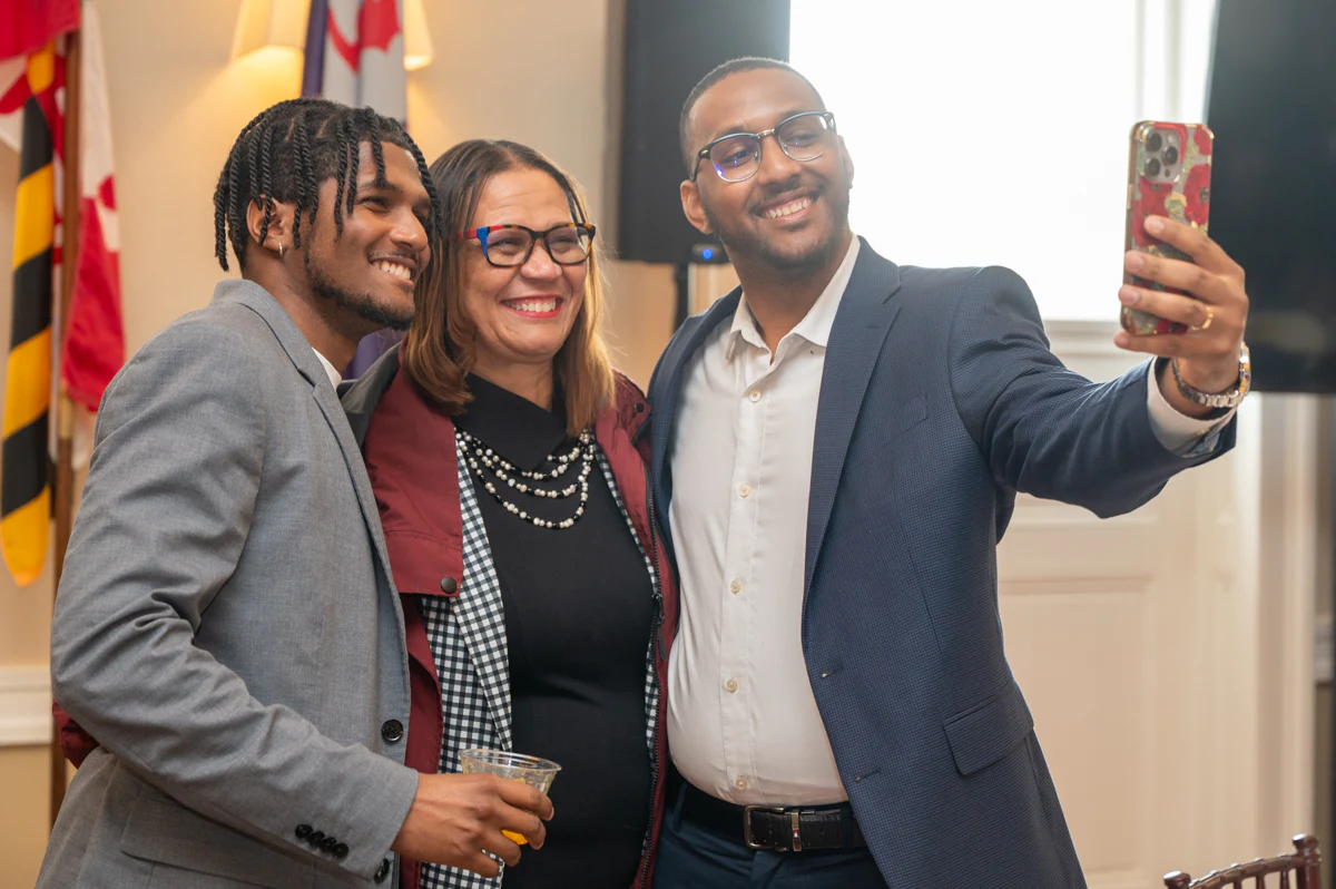Three people taking a selfie beside a flag at an event