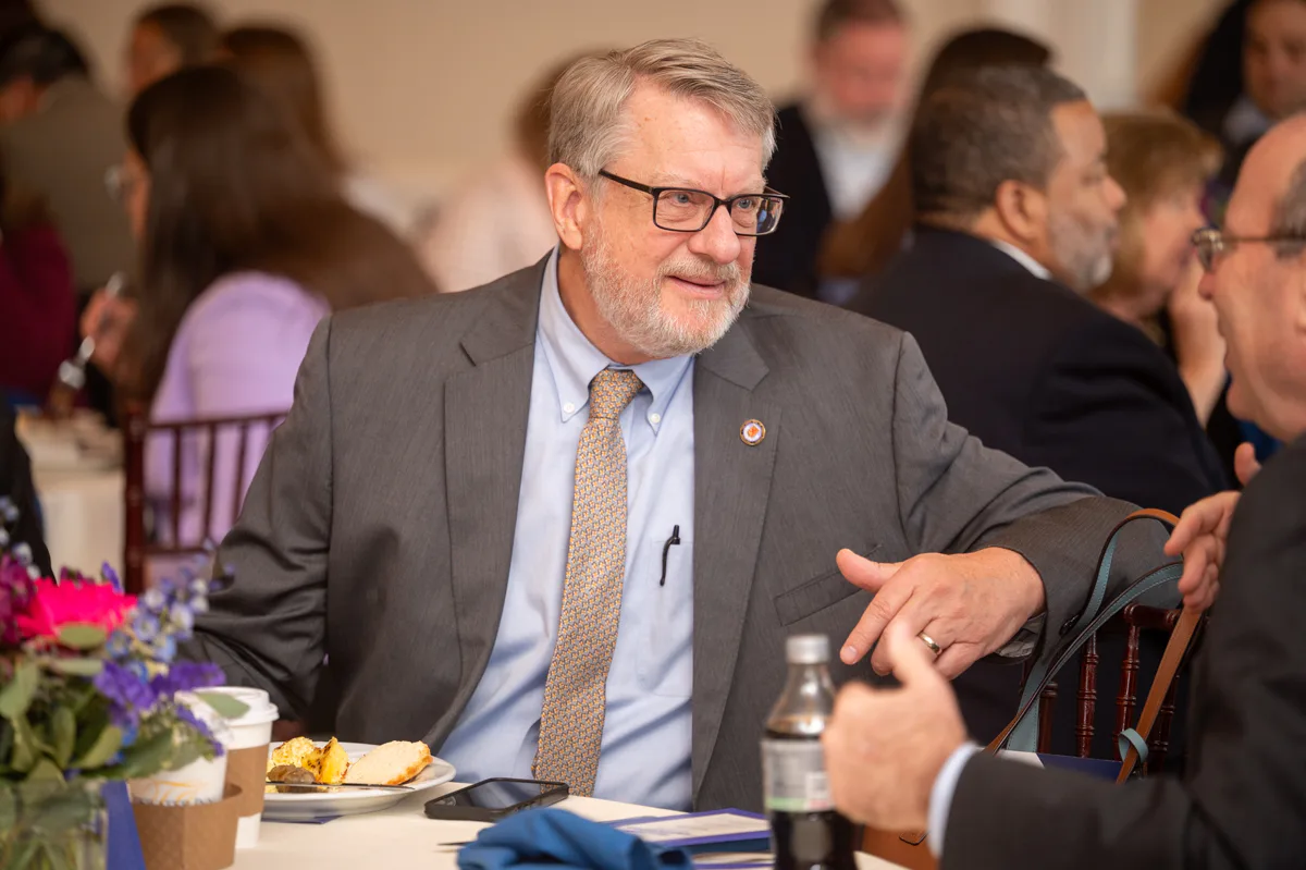 Man in gray suit with glasses seated at a banquet table