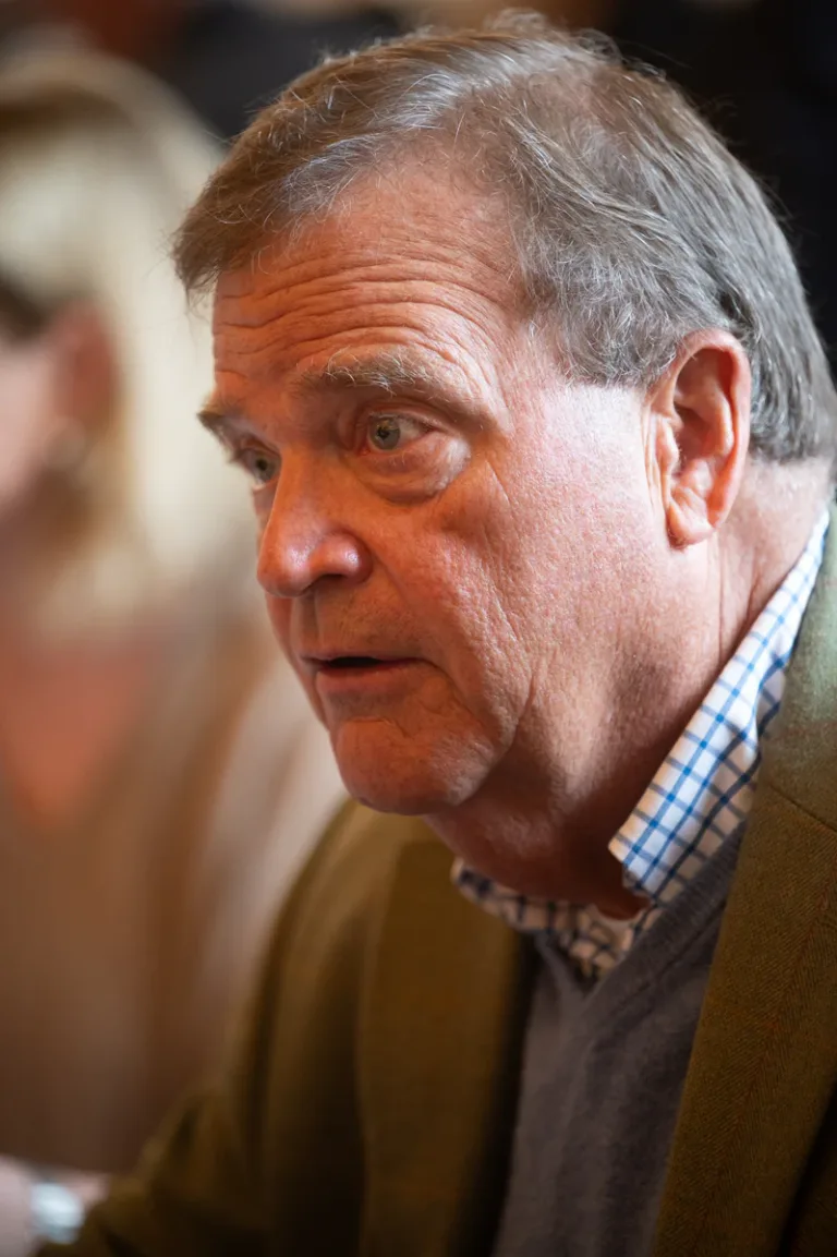 Older man with gray hair and plaid shirt looks toward the camera in a close-up