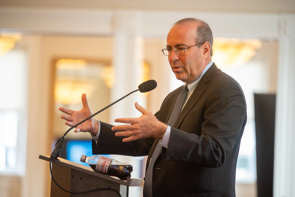 Man in dark suit gestures with both hands while speaking at a podium