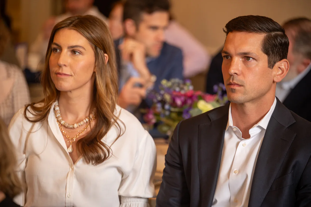 Woman in white blouse and man in dark suit sit attentively at an event
