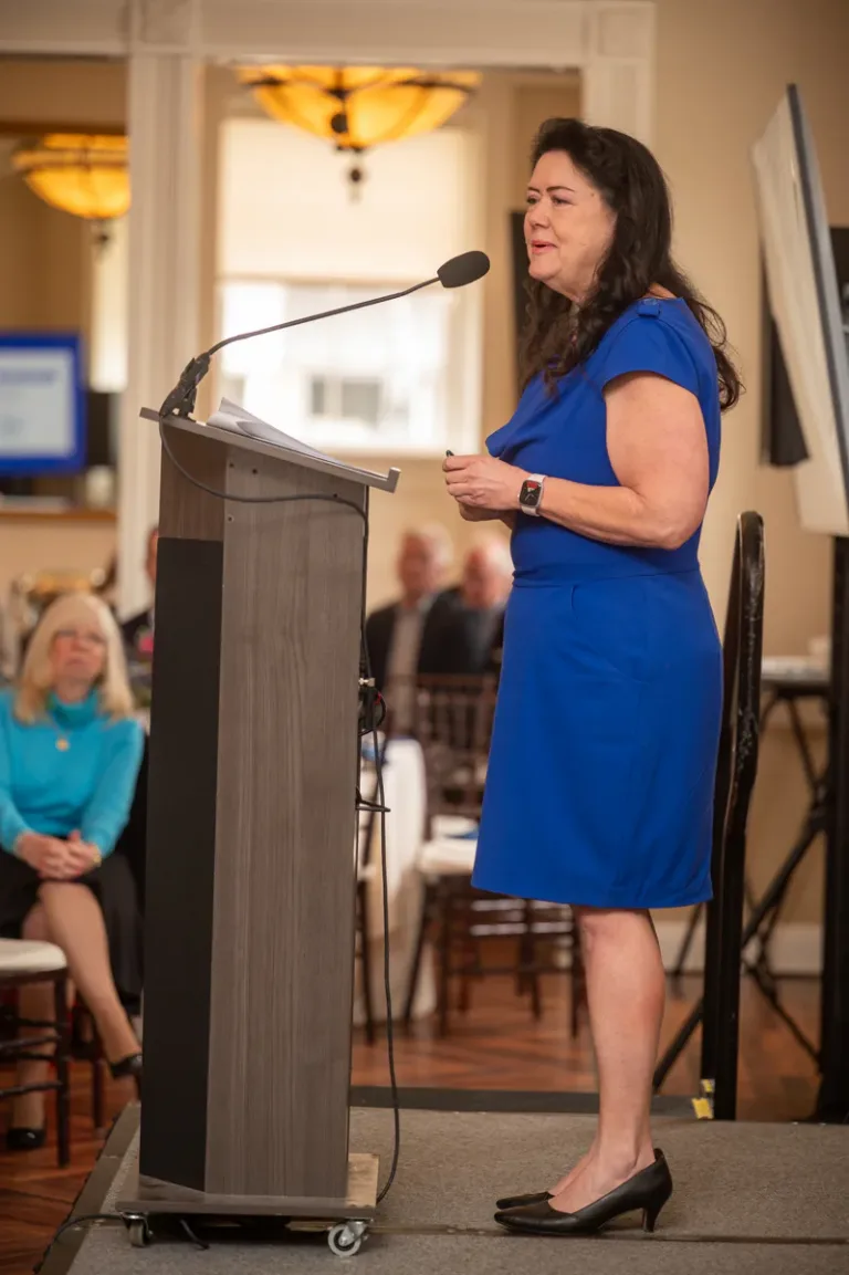 Woman in blue dress speaks at a wooden podium at an event
