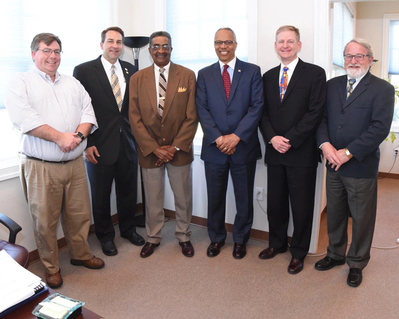 Six men in business attire posing together in an office