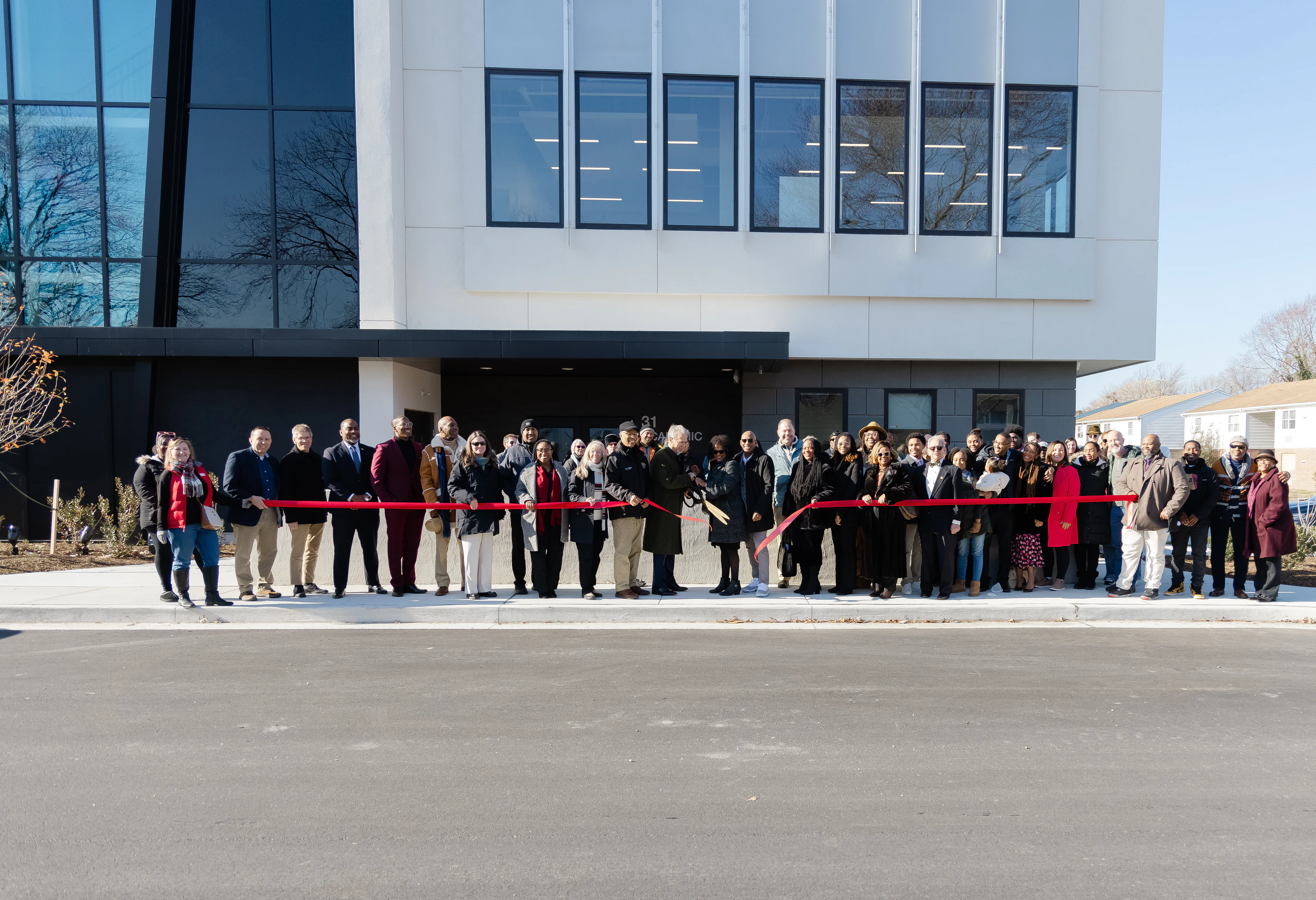 Large group of people holding a red ribbon at a ribbon cutting at a new building