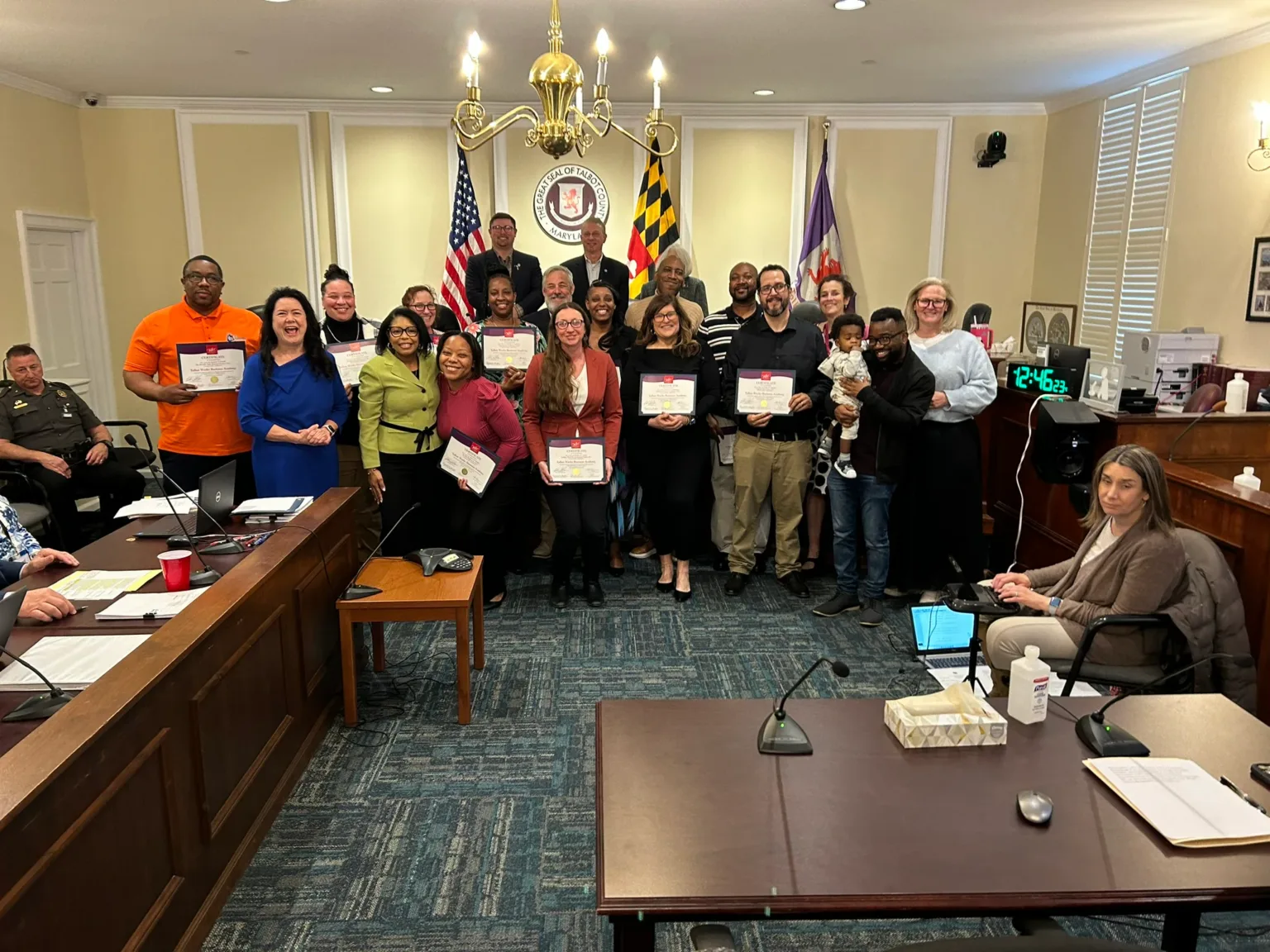 Group holding certificates standing in a council chamber with flags