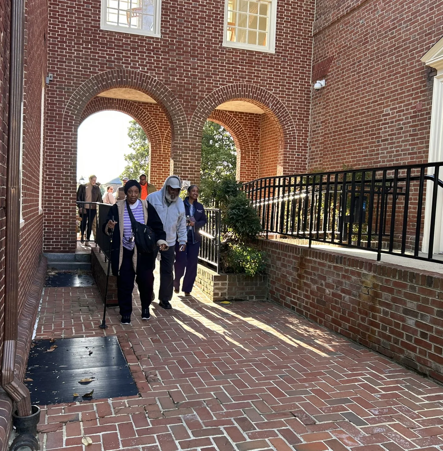Group of people walking along a brick walkway beneath arched doorways