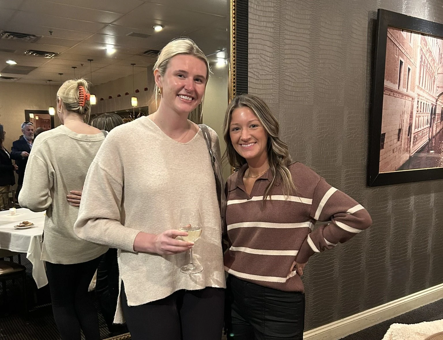 Two women smiling together at an event, one in a cream sweater