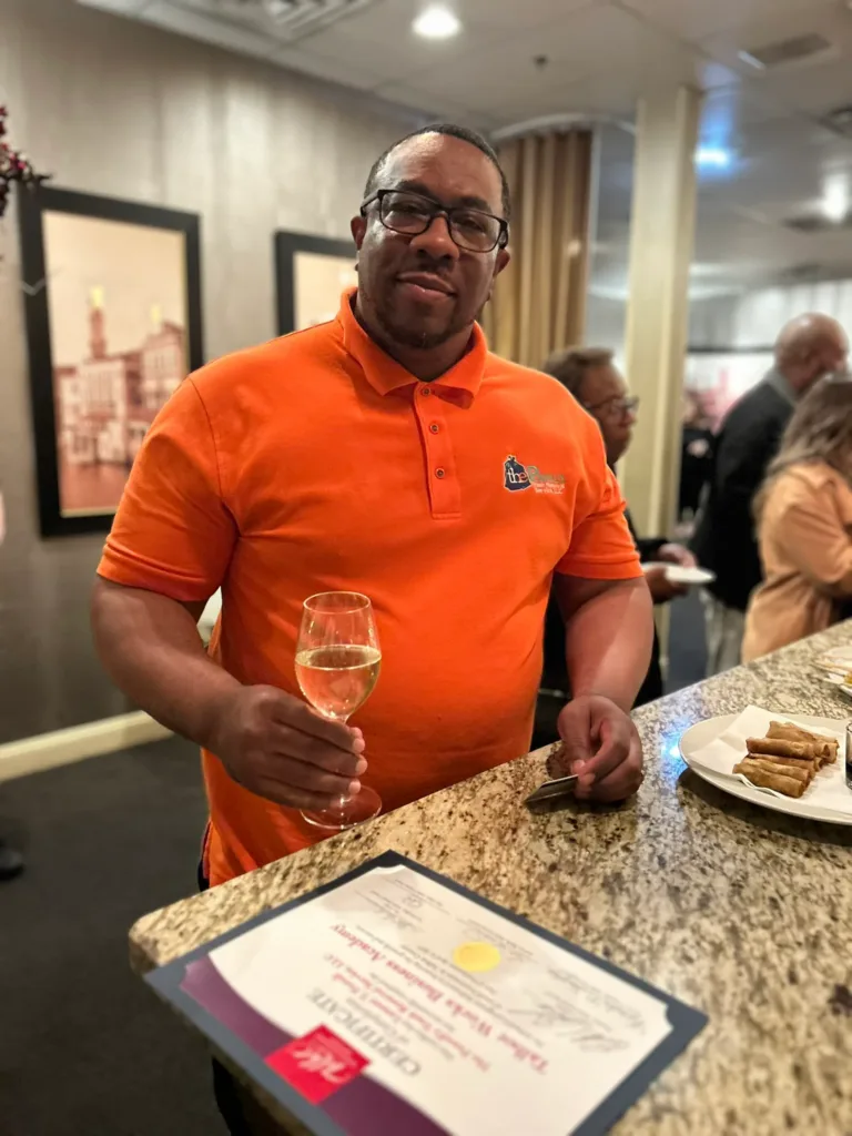 Man in orange polo holding a glass of sparkling wine at a reception
